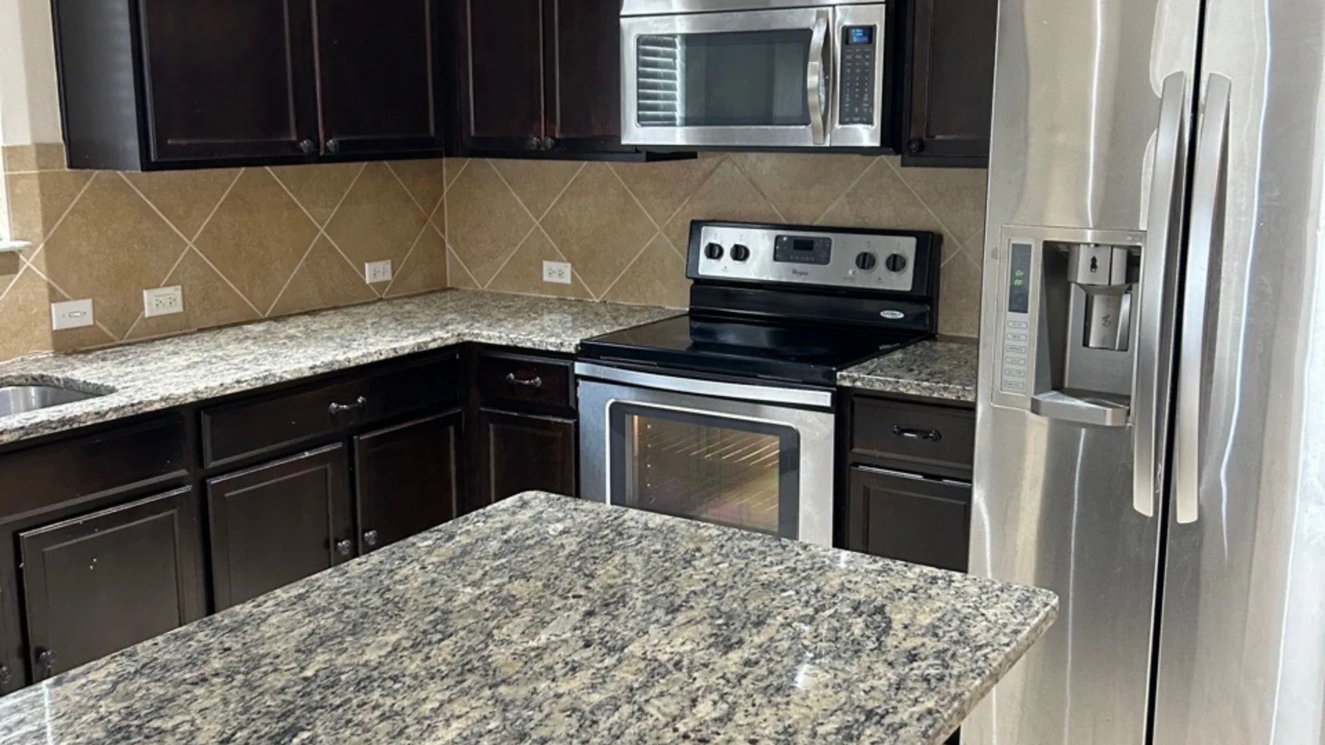 Spotless stainless steel refrigerator, microwave, and granite countertops in a home in Hutto, TX.