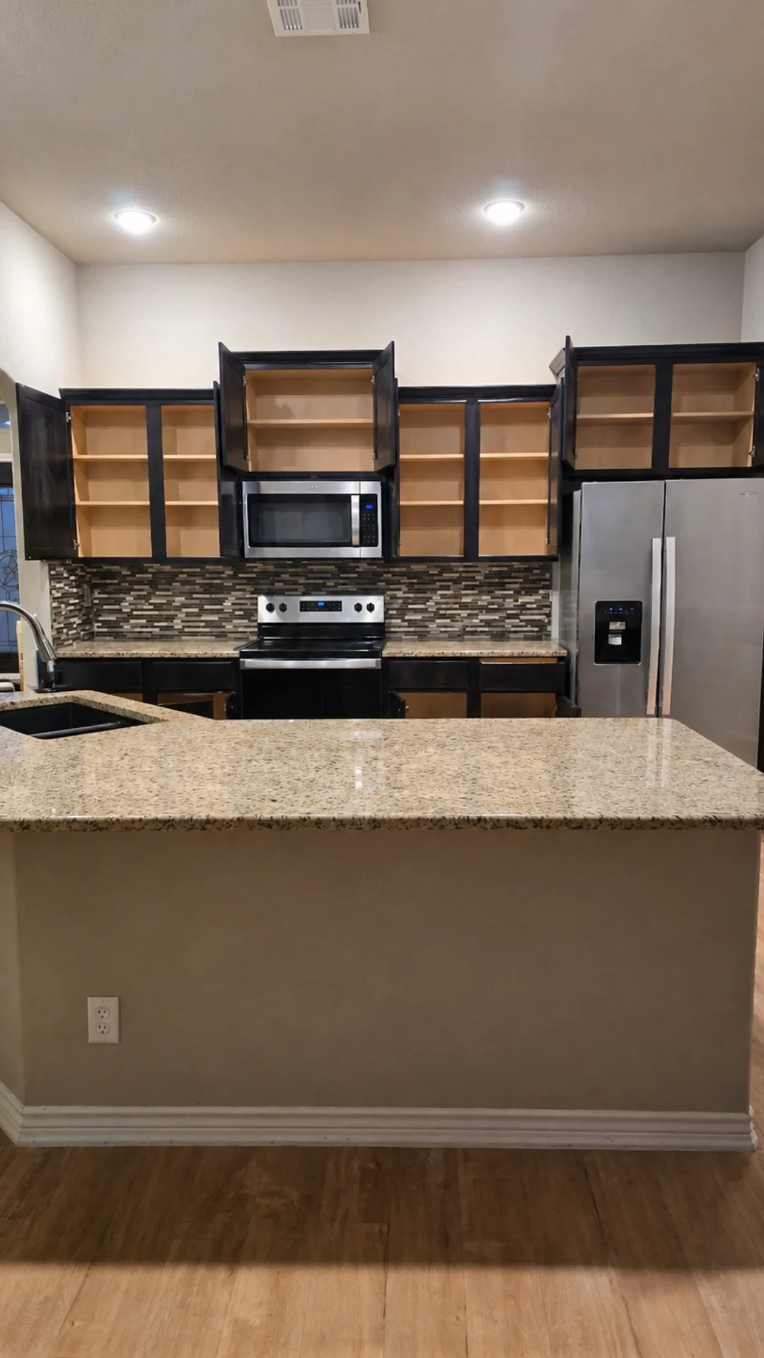 Empty open dark cabinets and granite countertops in a clean residential kitchen in Leander, TX.